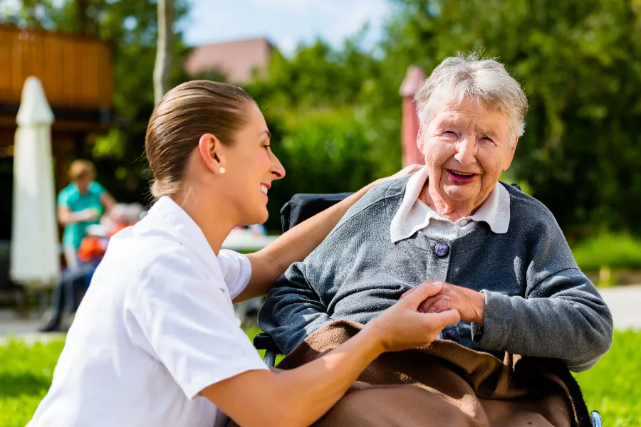 An older resident and her carer sharing a warm moment in a sunny garden.