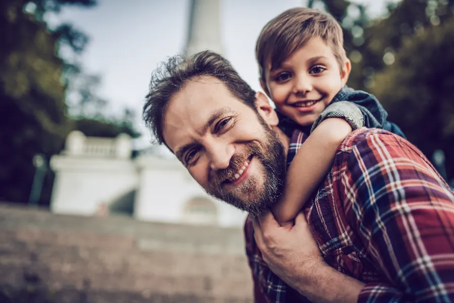 A father giving his son a piggyback in the sunshine — a young family on the way up.